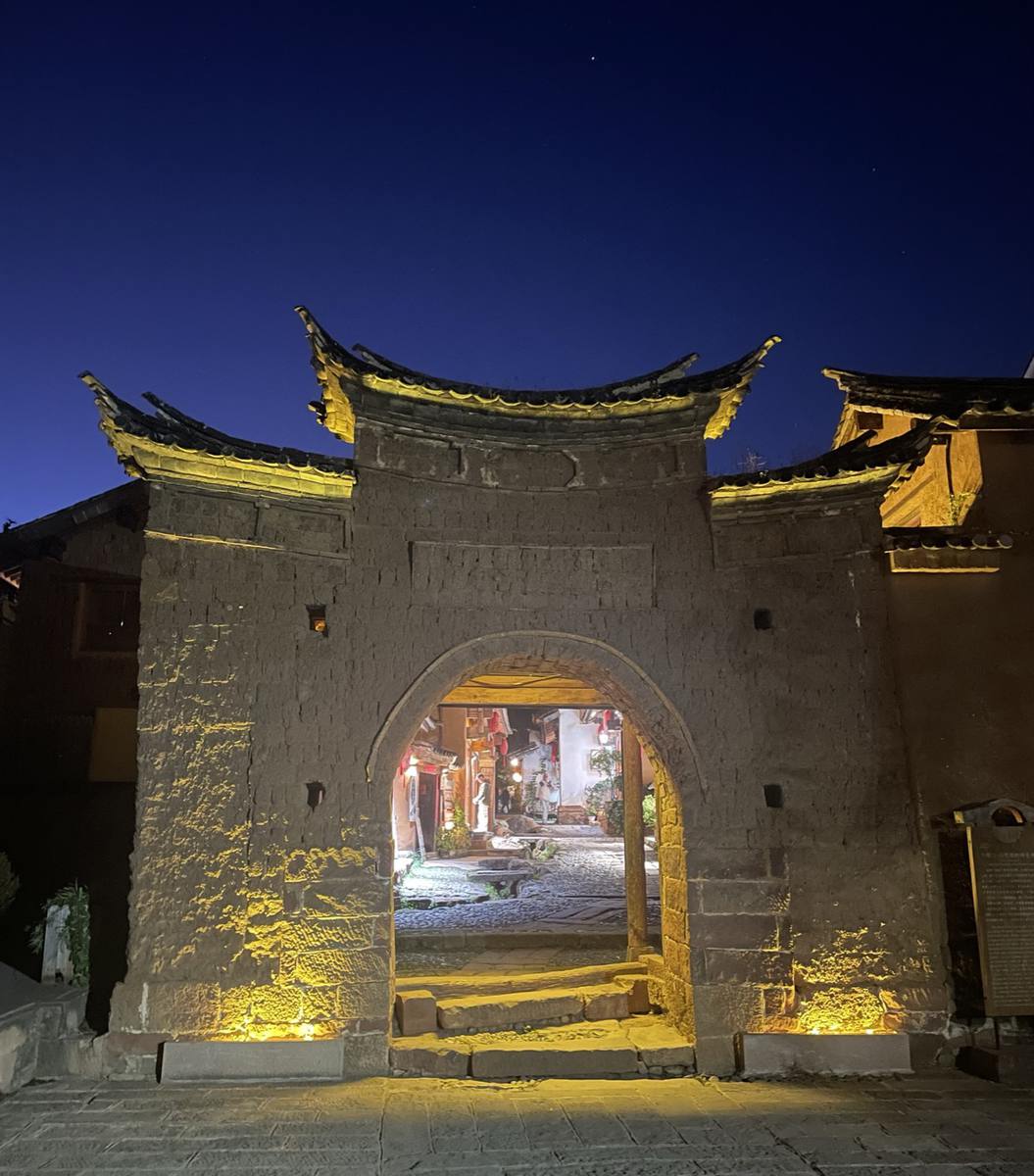 Shaxi's South Village Gate lit up at dusk, with Sideng Square visible through the archway